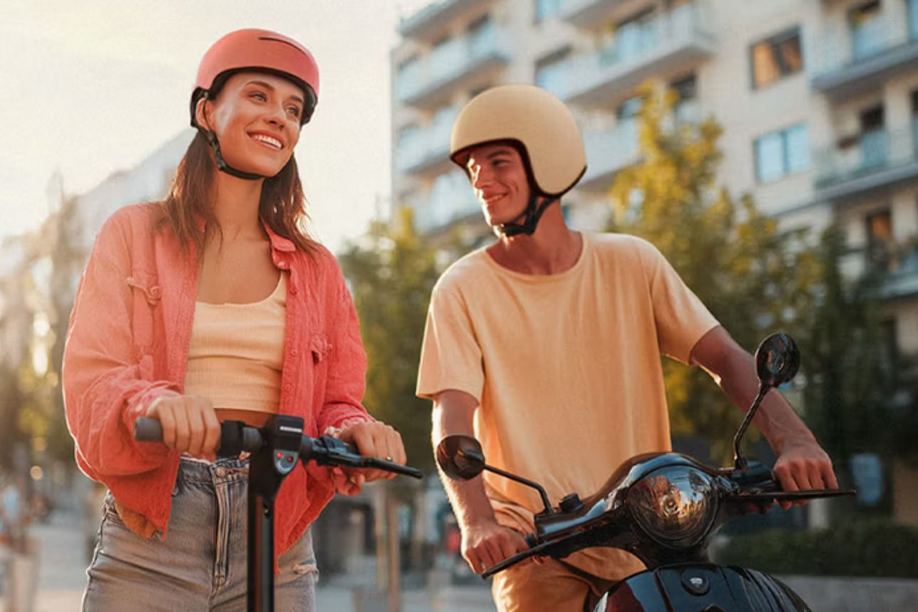 Eine Frau mit Helm mit einem eScooter und ein Mann mit Helm auf einem Roller
