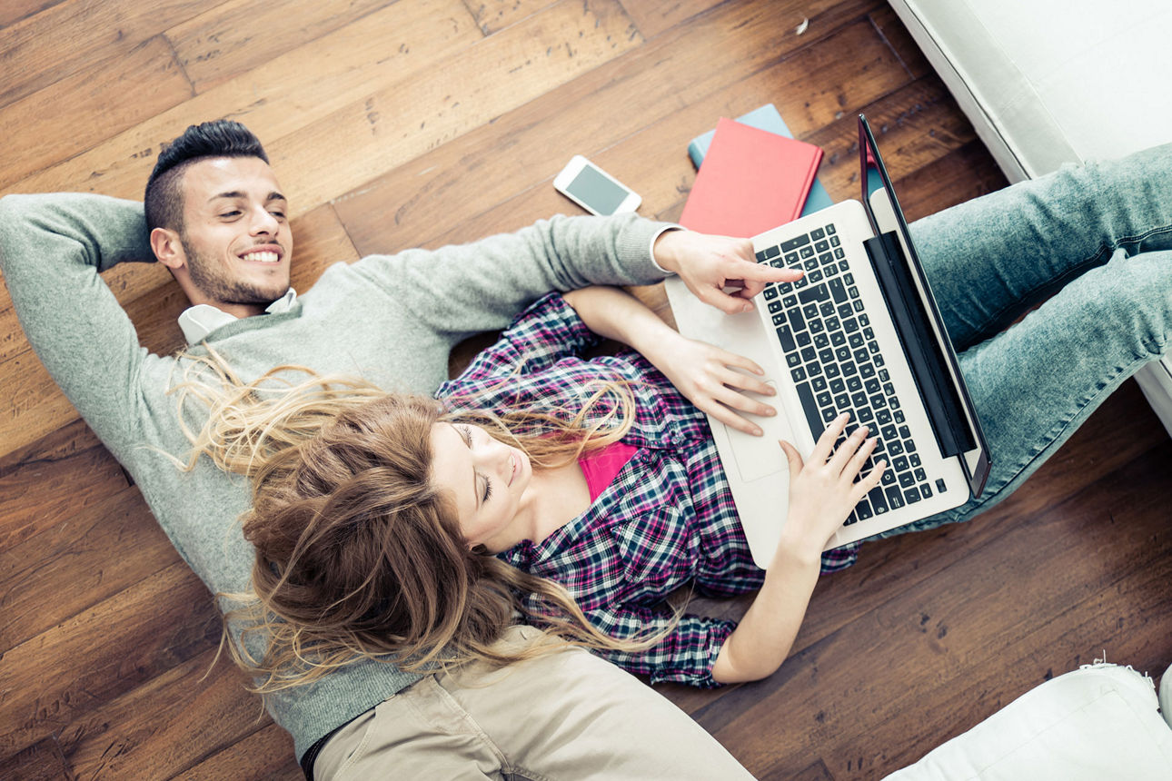 Mann und Frau liegen auf dem Boden und schauen in den Laptop
