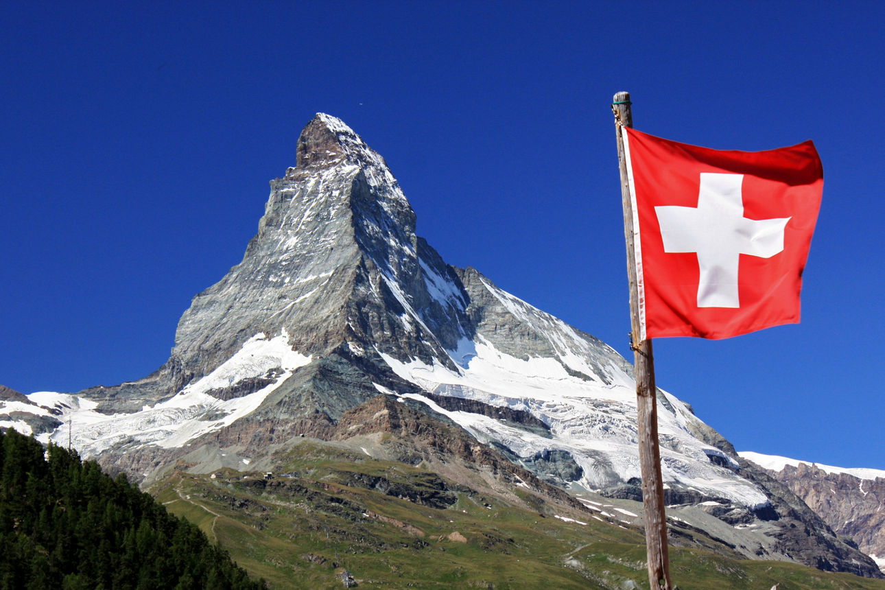 Das Matterhorn in der Schweiz vor einem blauen Himmel. Im Vordergrund weht die Schweizer Flagge.