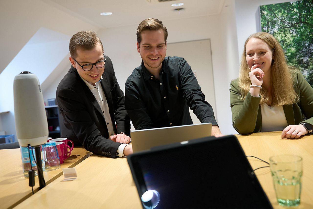 Zwei Männer und eine Frau schauen auf einen Laptop