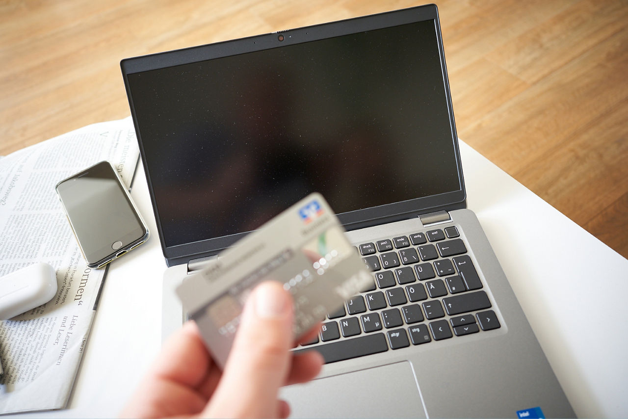 Hand hält eine Visa-Card vor einem Computer.