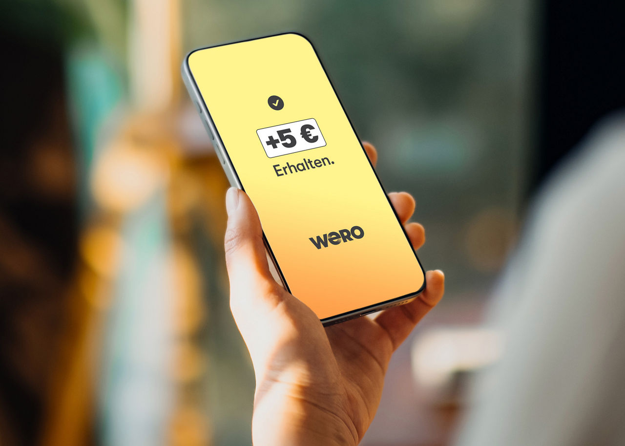 Hand mit Handy. Auf dem Display ist +5€ zu lesen