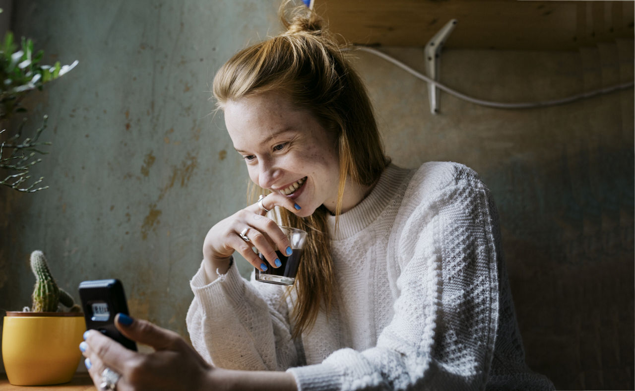 Frau sitzt an Tisch und schaut auf ihr Smartphone