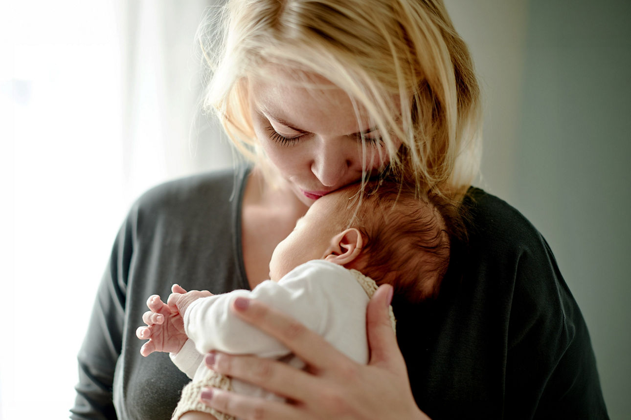 Mutter hält ihr Baby im Arm und küsst es auf die Stirn