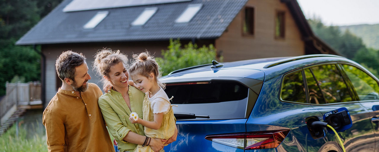 Junge Familie vor dem Eigenheim mit Photovoltaik und E-Ladestation