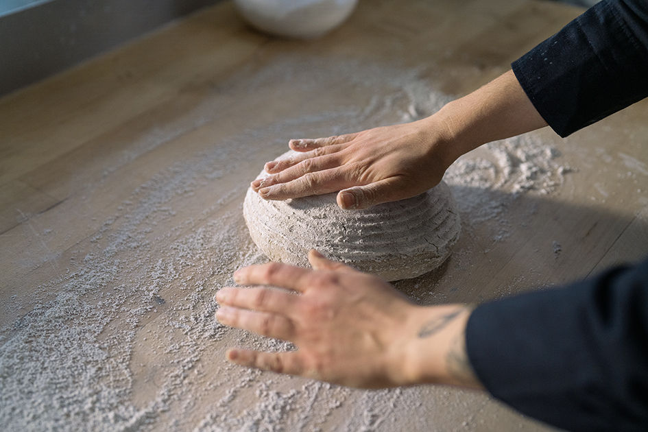 Auf einer bemehlten Arbeitsplatte wird ein Brotlaib von zwei Händen geformt