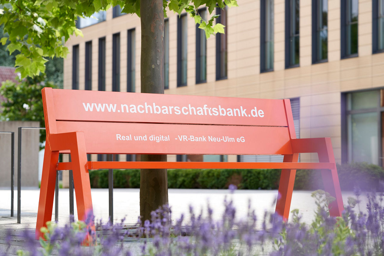 Eine orange Bank vor dem Bankgebäude in Weißenhorn