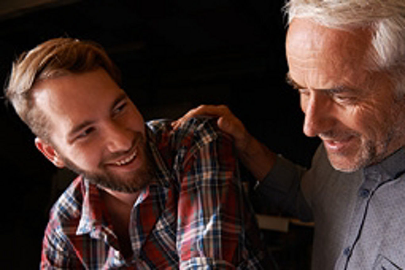 Ein lächelnder Mann steht neben einem anderen Mann, beide wirken freundlich