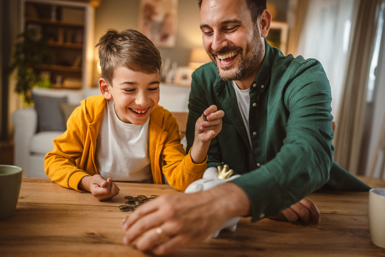 Der Vater und sein Sohn sammeln Münzen ein und werfen sie in ein Sparschwein.
