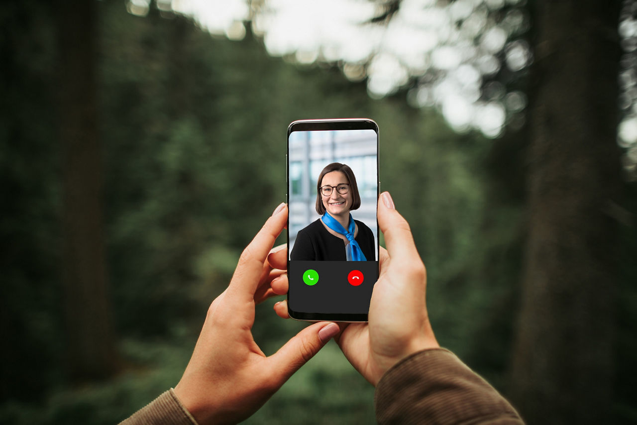 Hände halten ein Handy mit einem Videoanruf im Wald