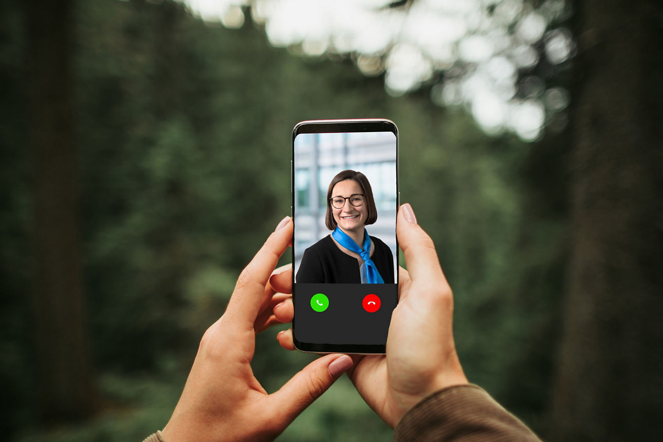 Hände halten ein Handy mit einem Videoanruf im Wald