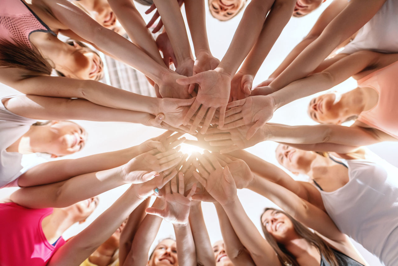 Abbildung zeigt mehrere Personen, die als Zeichen von Teamgeist ihre Hände zusammenhalten