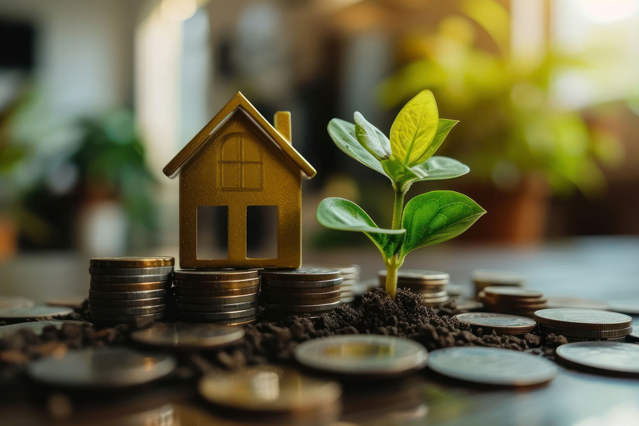 Ein kleines Hausmodell, Münzen und eine wachsende Pflanze symbolisieren gemeinsam nachhaltige Investitionen, Immobilienfinanz