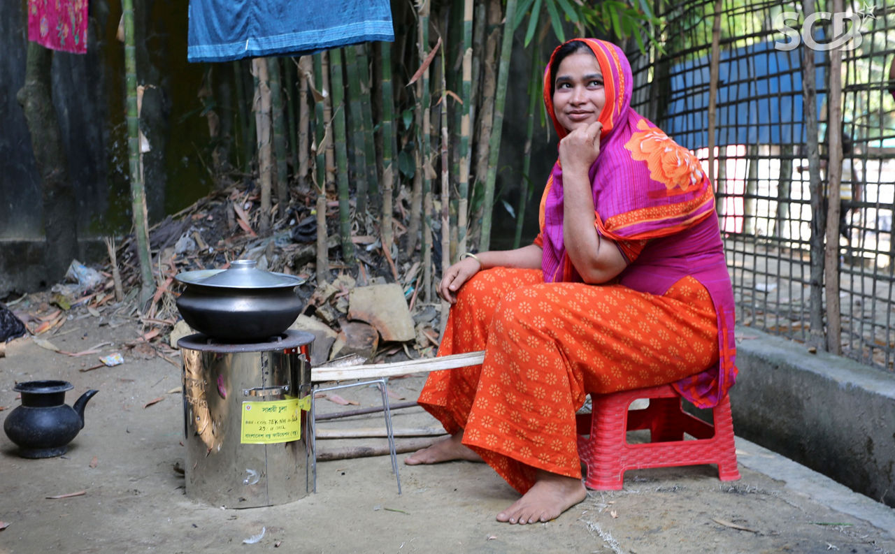Eine Frau in Bangladesch sitzt draußen vor einem Kochofen.