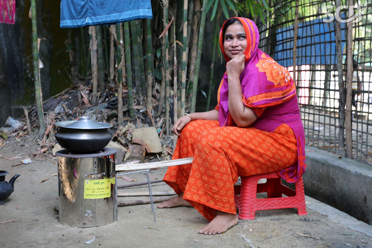 Eine Frau in Bangladesch sitzt draußen vor einem Kochofen.