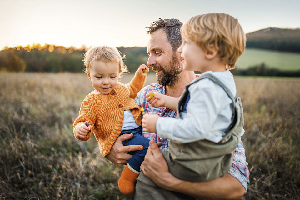 Vater trägt seine beiden Kinder durch ein Getreidefeld