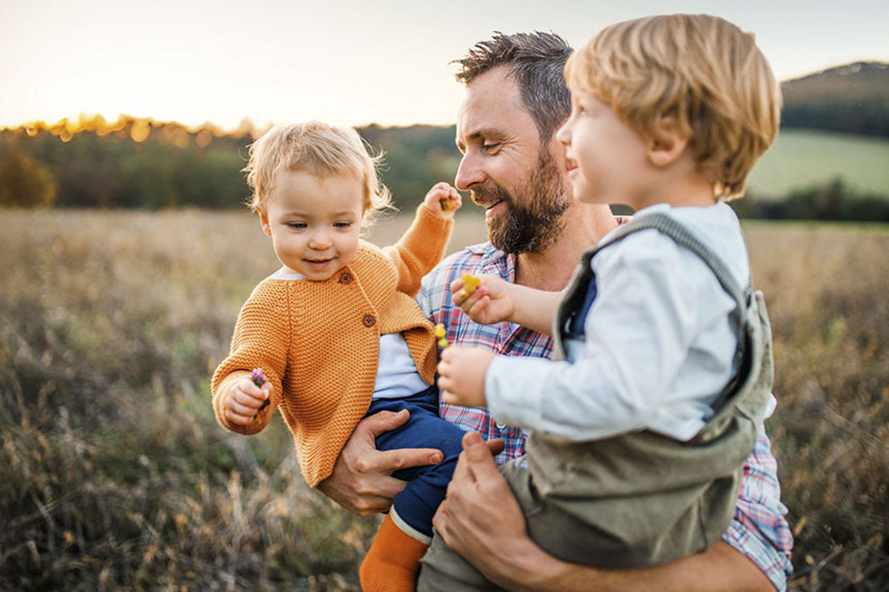 Vater trägt seine beiden Kinder durch ein Getreidefeld