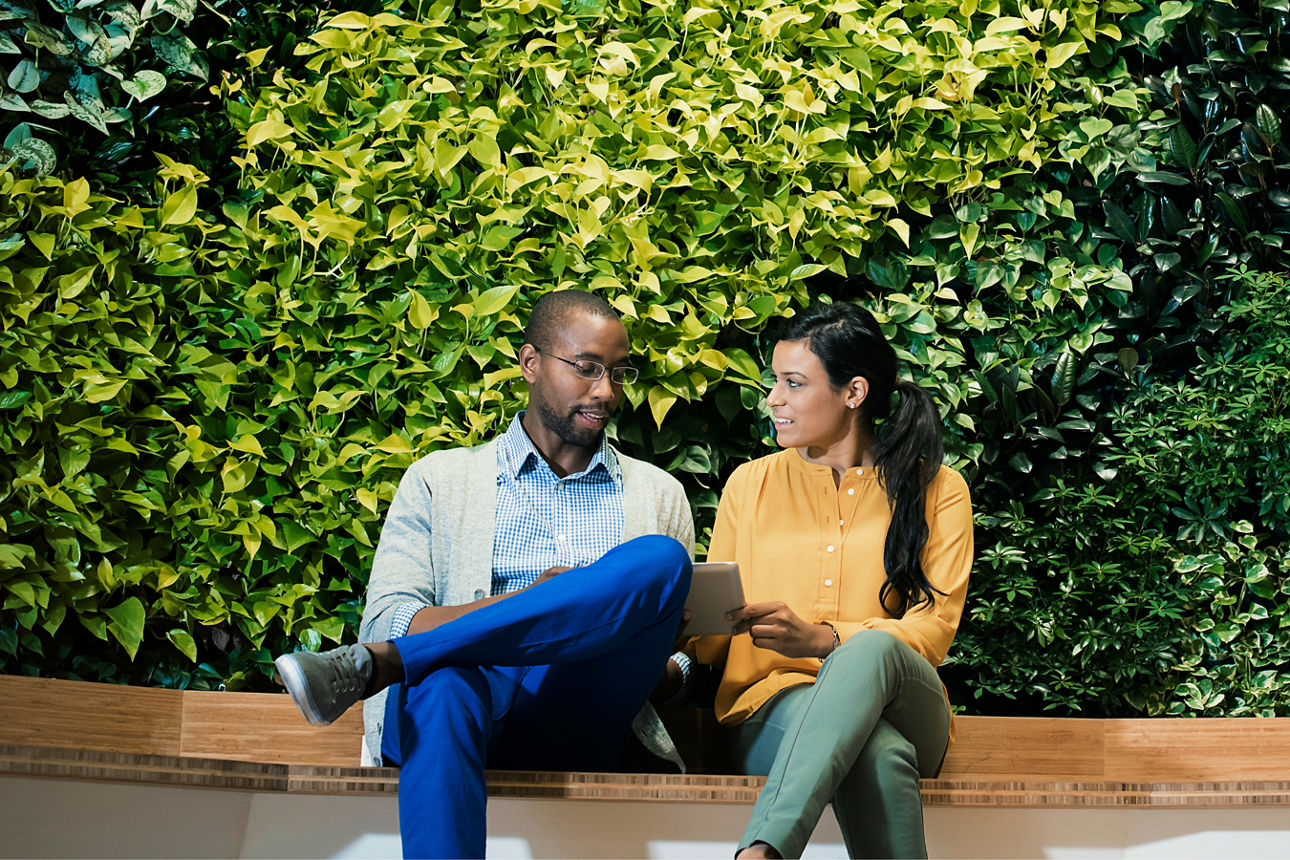 Ein Mann und eine Frau sitzen auf einer Holzbank vor einer Hecke