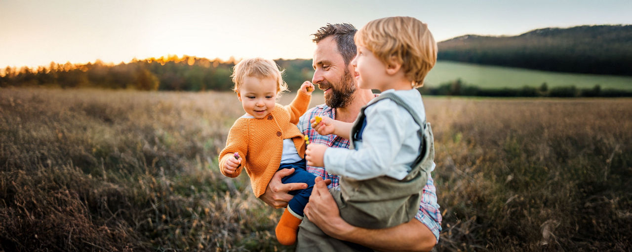 Vater trägt seine beiden Kinder durch ein Getreidefeld