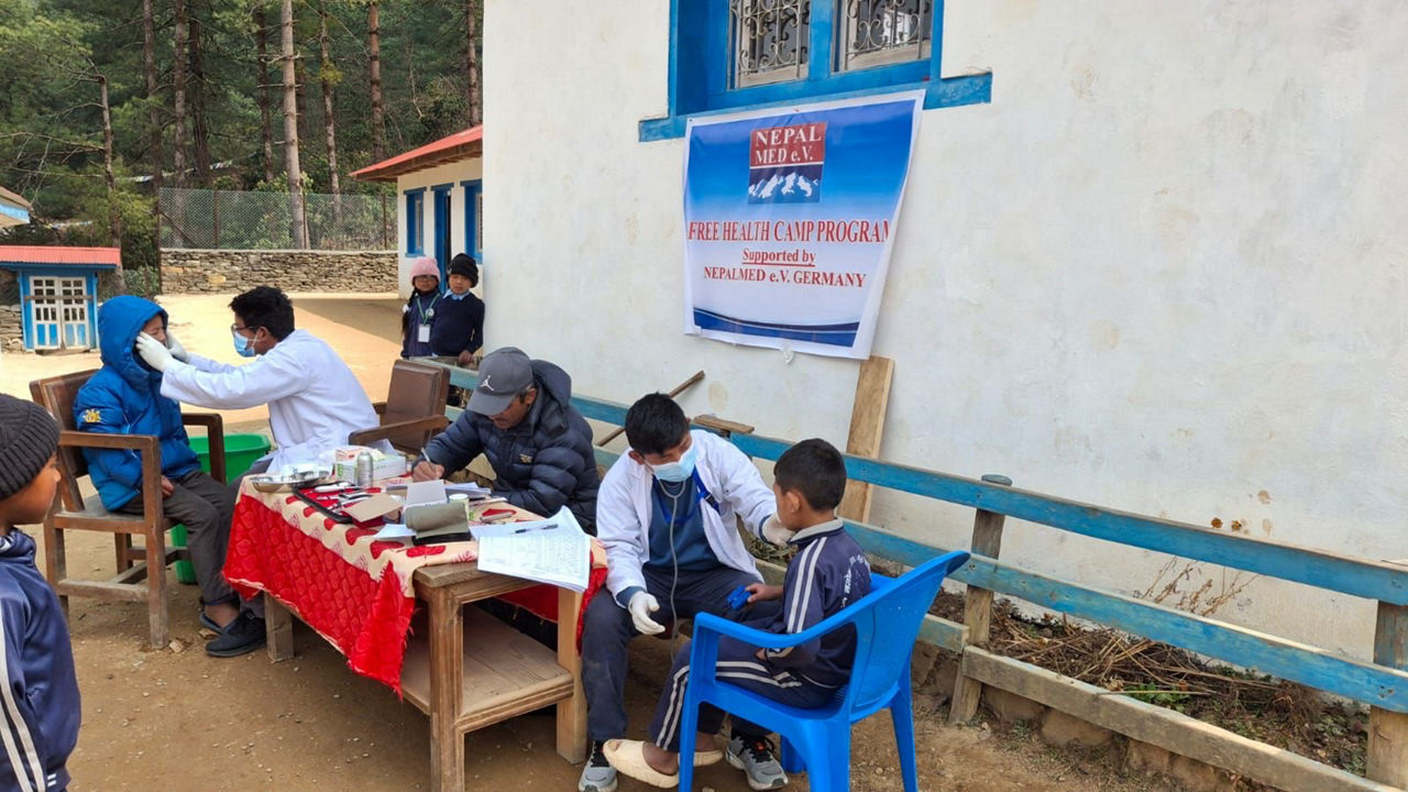 Mehrere ehrenamtlich Helfer medizinische Helfer versorgen Kinder. Hinter ihnen ist ein Banner des Nepalmed e.V.