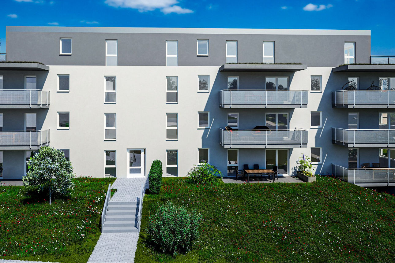 Modernes Mehrfamilienhaus mit Balkonen und großen Fenstern, umgeben von einer grünen Wiese