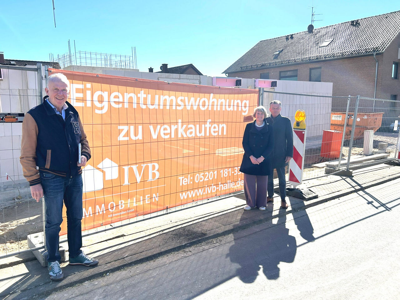 Drei Personen stehen am Baugelände - im Hintergrund ein Werbeschild zur Baumaßnahme