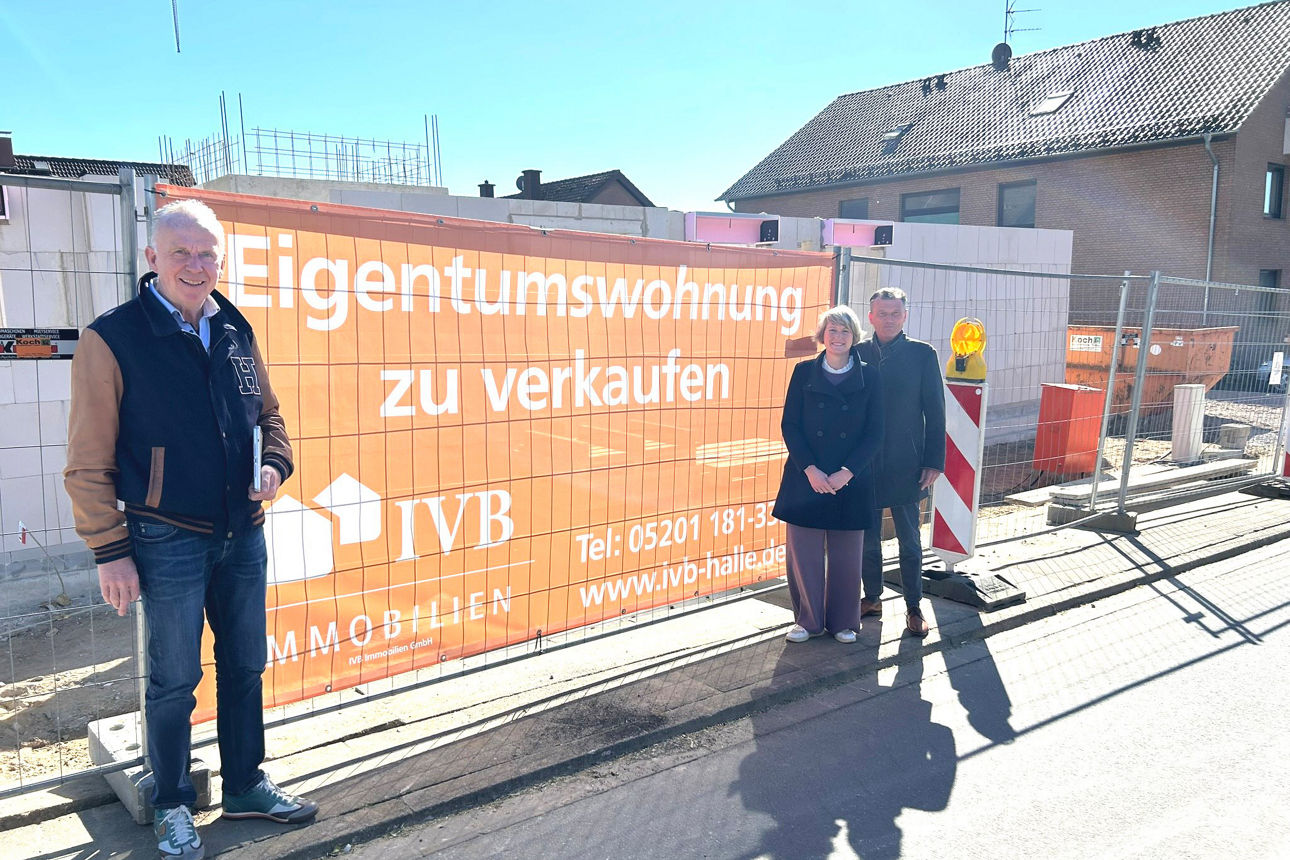 Drei Personen stehen am Baugelände - im Hintergrund ein Werbeschild zur Baumaßnahme