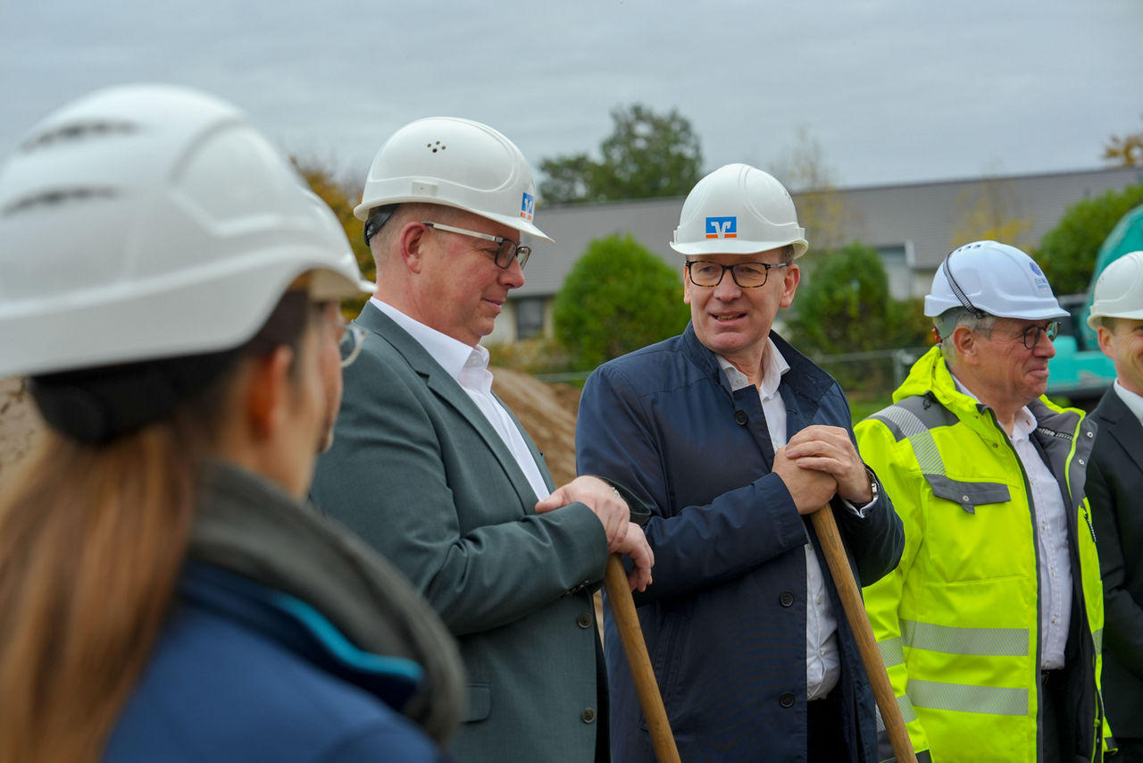 Vier Personen in Nahaufnahme auf derselben Baustelle. Alle tragen weiße Schutzhelme.