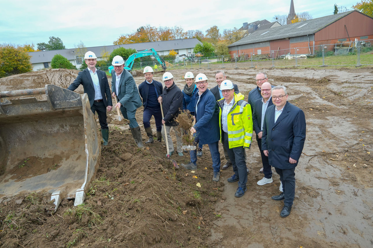 Das Foto zeigt eine Gruppe von elf Personen auf einer Baustelle. Alle tragen Schutzhelme, einige außerdem Gummistiefel.