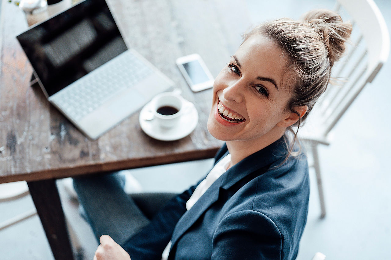 Abbildung zeigt eine fröhliche Frau mit Kaffee, die gerade am Laptop ihr Konto zu Meine Bank gewechselt hat.