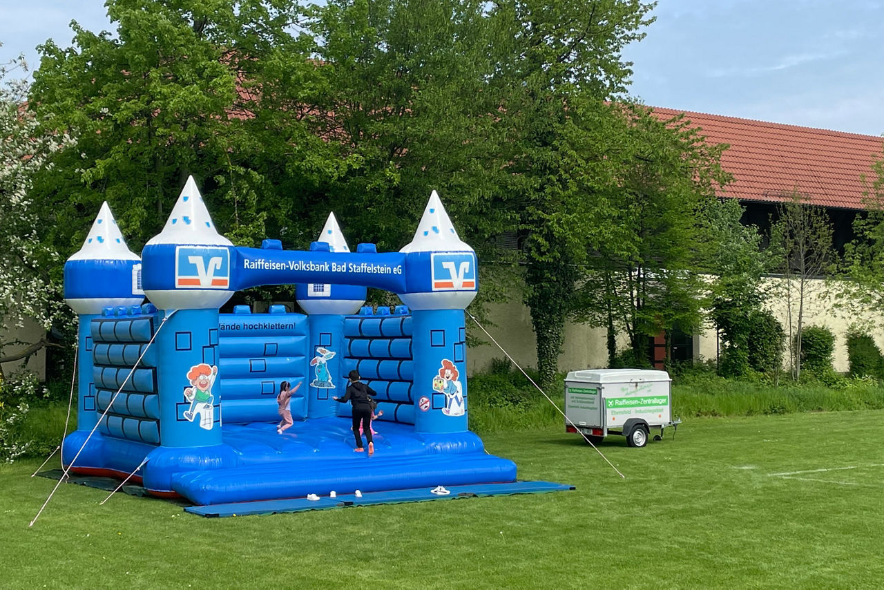 Ein leuchtend blaues, aufblasbares Schloss, als Hüpfburg steht auf einer grünen Wiese 