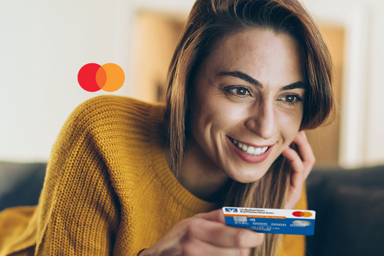 Frau liegt auf einer Couch und hat in ihrere Hand eine Kreditkarte. Sie blickt dabei in eine Laptop.