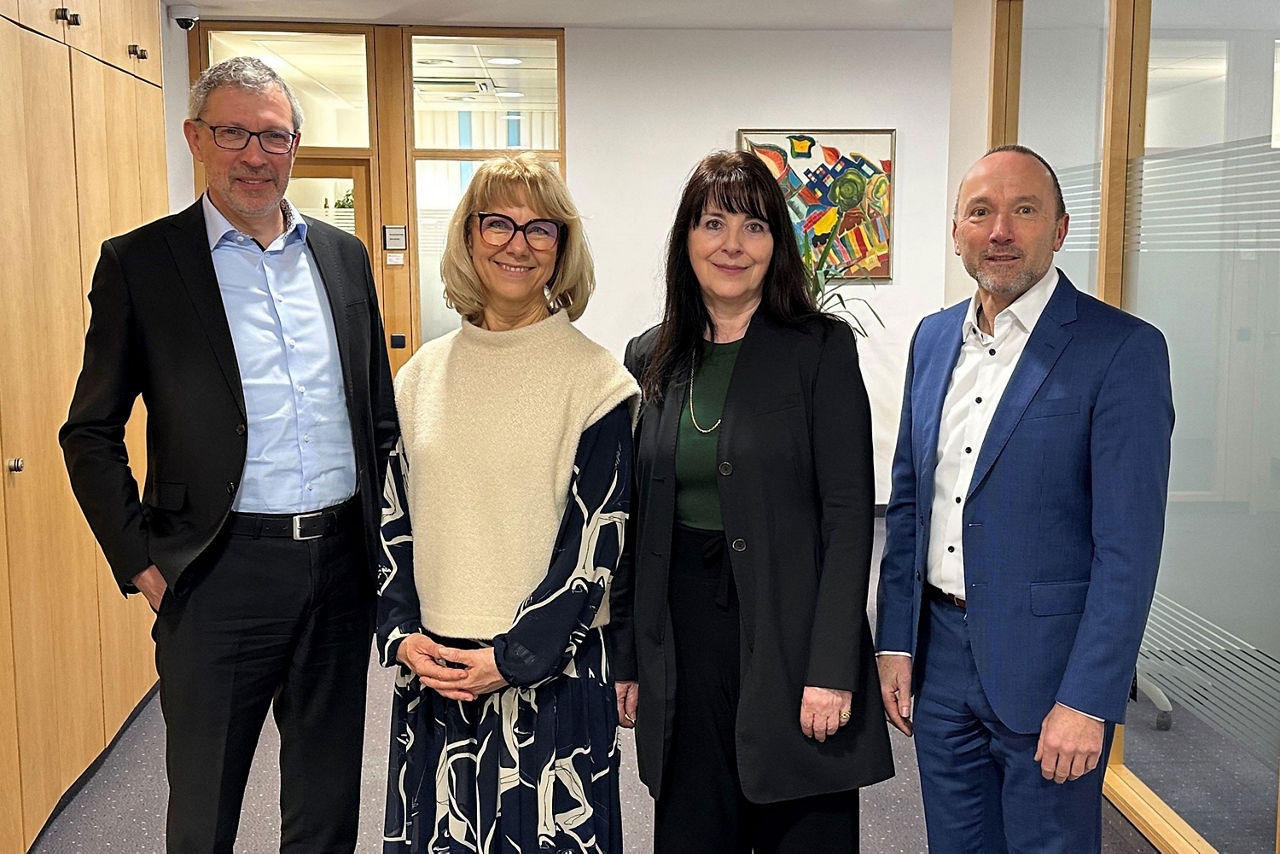 zwei Frauen und zwei Männer in einem Bürogebäude blicken gemeinsam in die Kamera