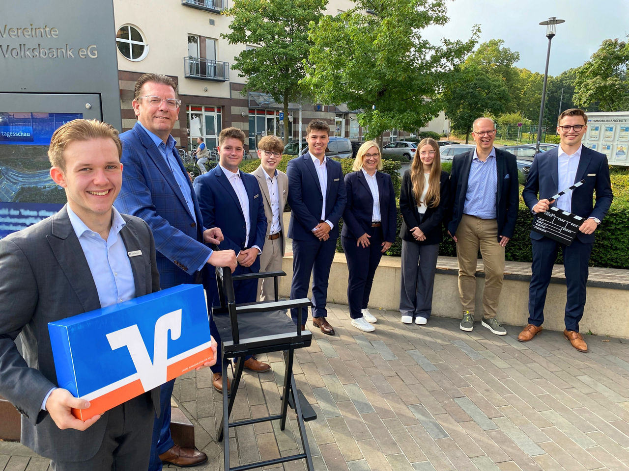 Sechs neue Azubis stehen mir Mitarbeitern vor dem Gebäude der Vereinten Volksbank