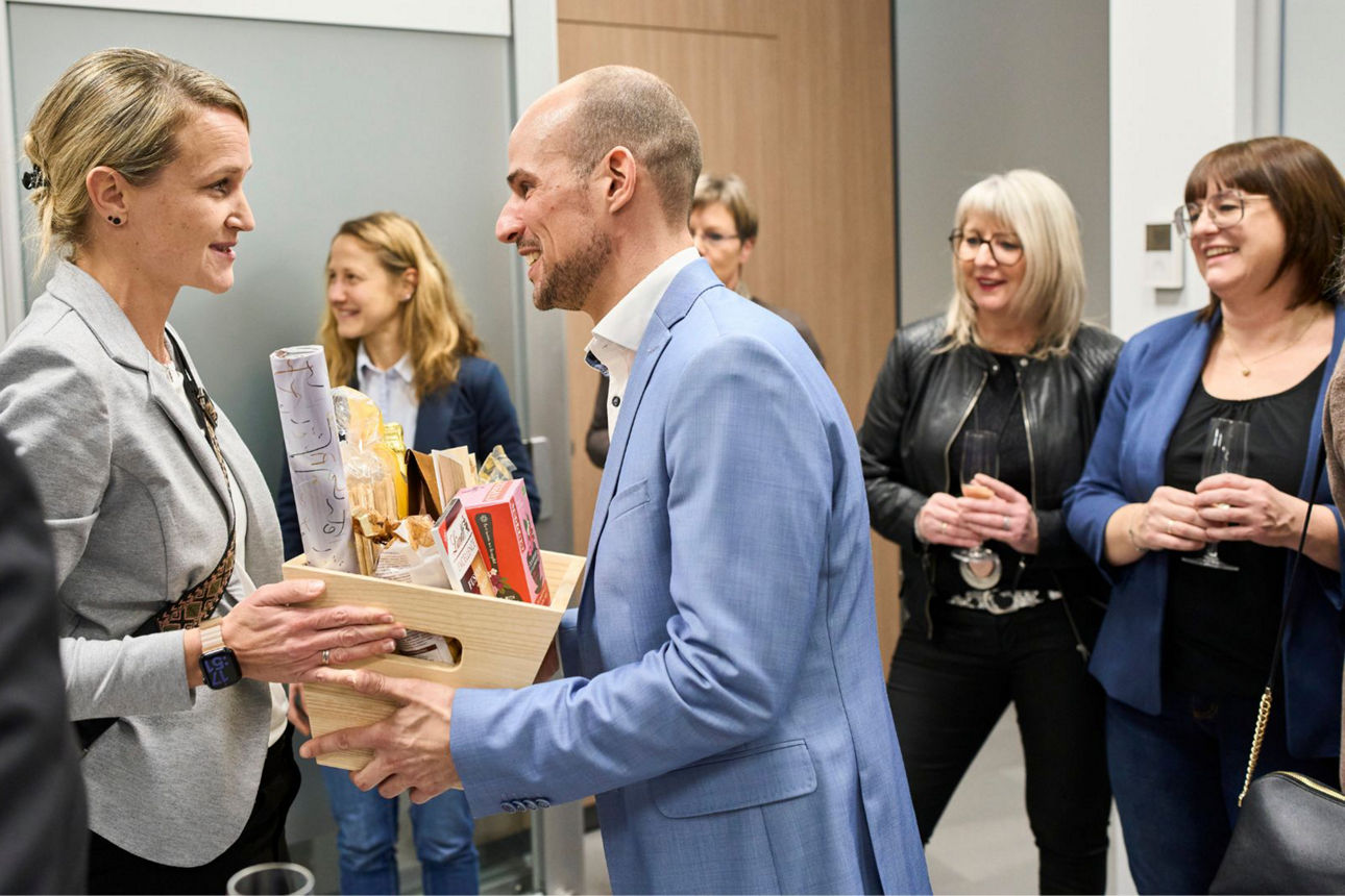 Das Bild zeigt Planerin Sandra Kiefer-Weber bei der Übergabe eines Geschenkkorbs an Filialleiter Simon Schell