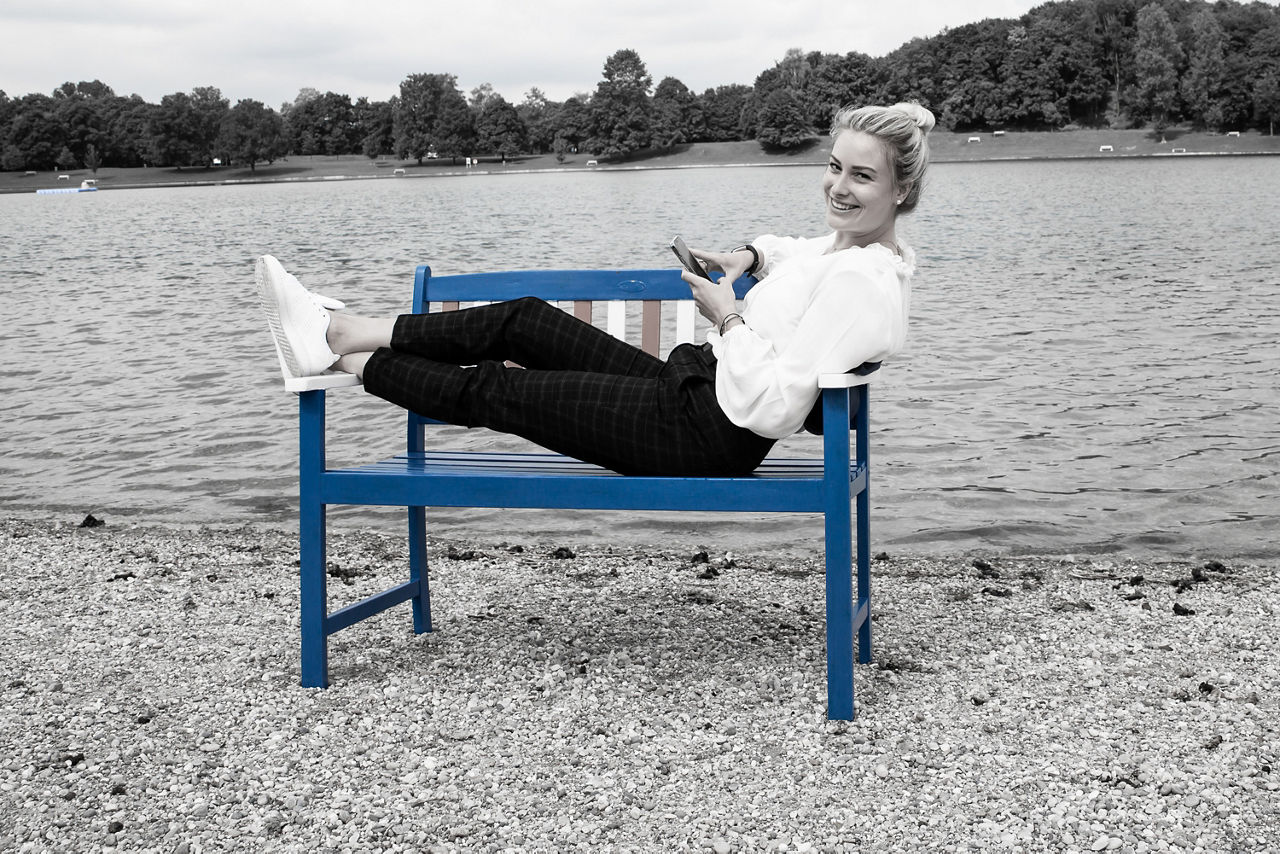 Frau liegt auf einer Holzbank am Ufer eines Sees
