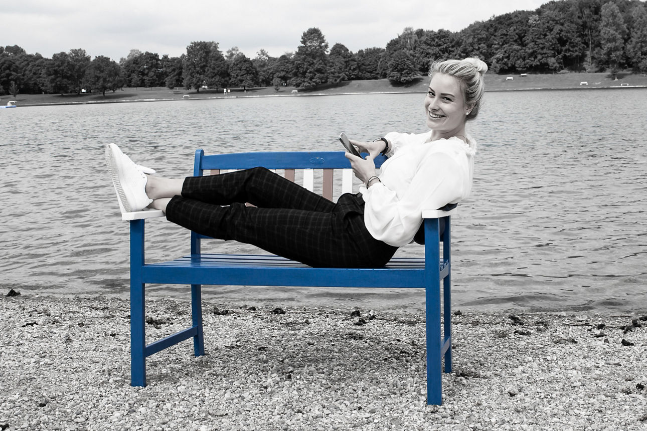 Frau liegt auf einer Holzbank am Ufer eines Sees