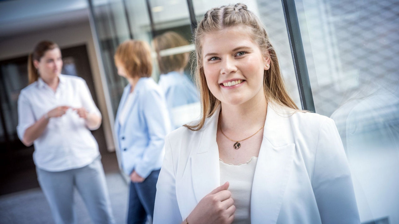 Eine junge Frau steht im Vordergrund, dahinter 2 weitere Kolleginnen im Gespräch.