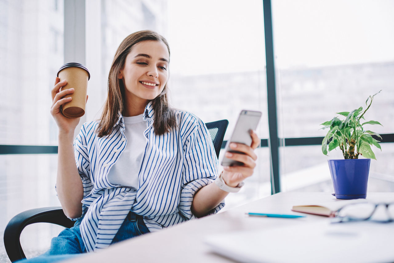 Junge Frau mit Kaffeebecher und Handy in der Hand