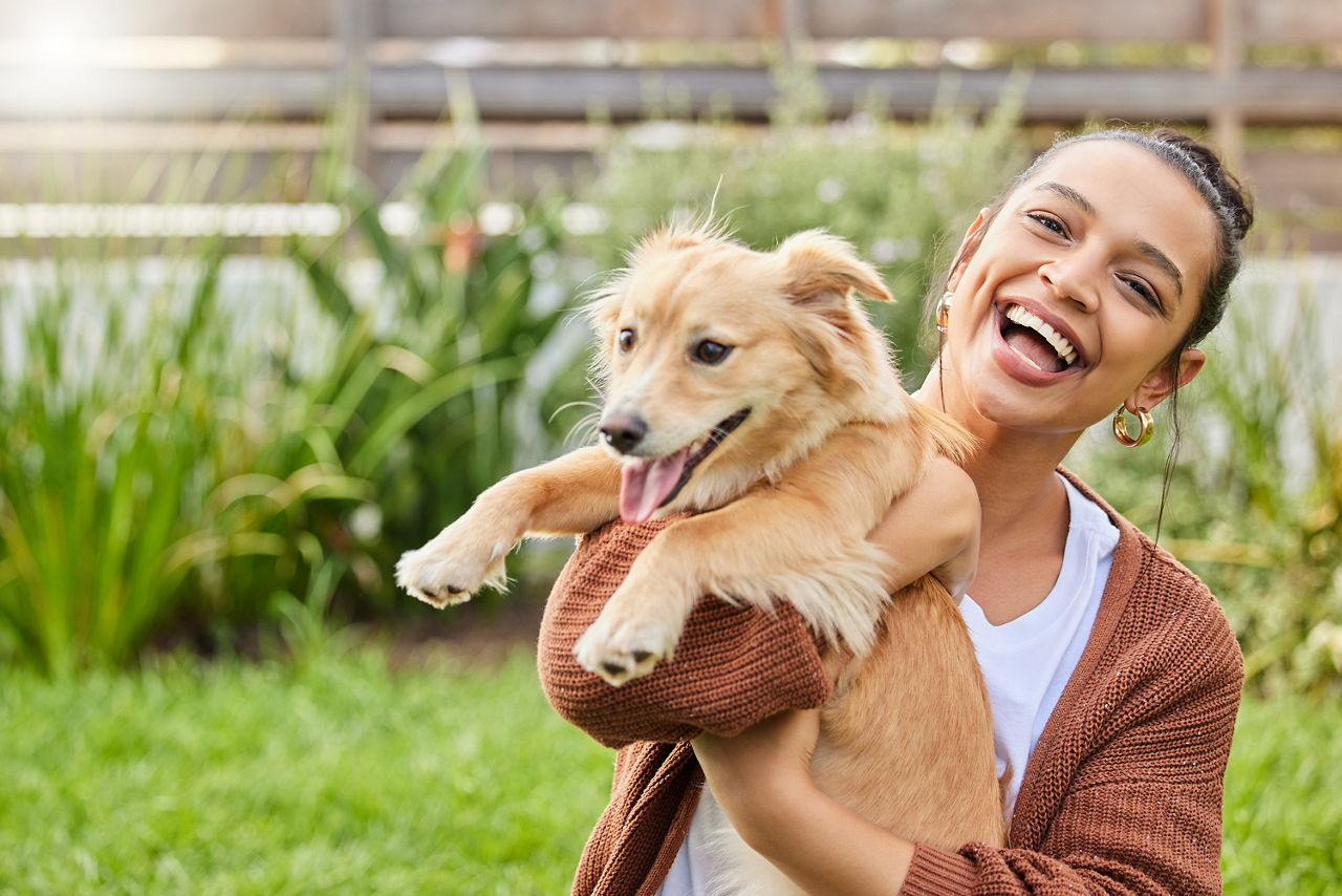 Porträt einer attraktiven jungen Frau, die spielerisch ihren Hund im Garten hält.