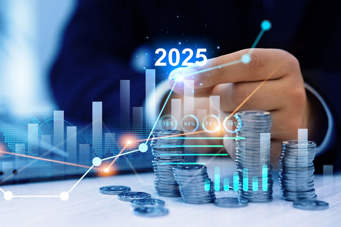 Mehrere Münzstapel und Wertpapierkurse. Dahinter die Hand eines Mannes und die Jahreszhal "2025"