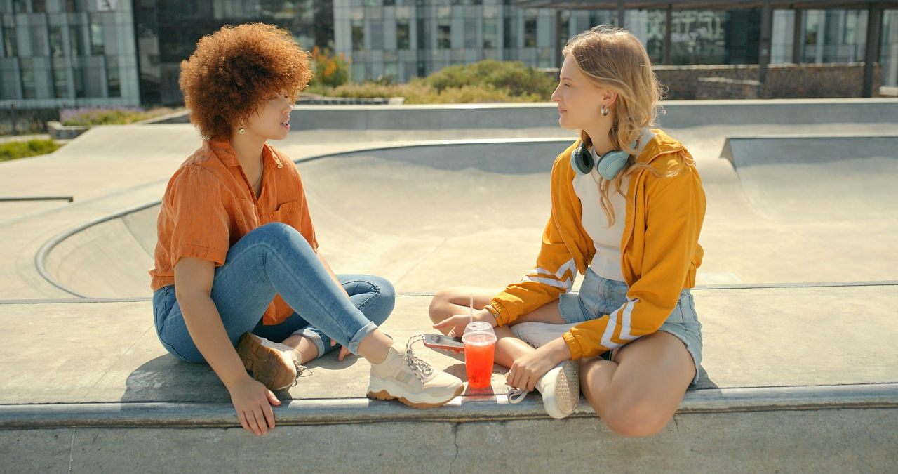 Zwei junge Frauen, die sich bei einem Skatepark unterhalten.