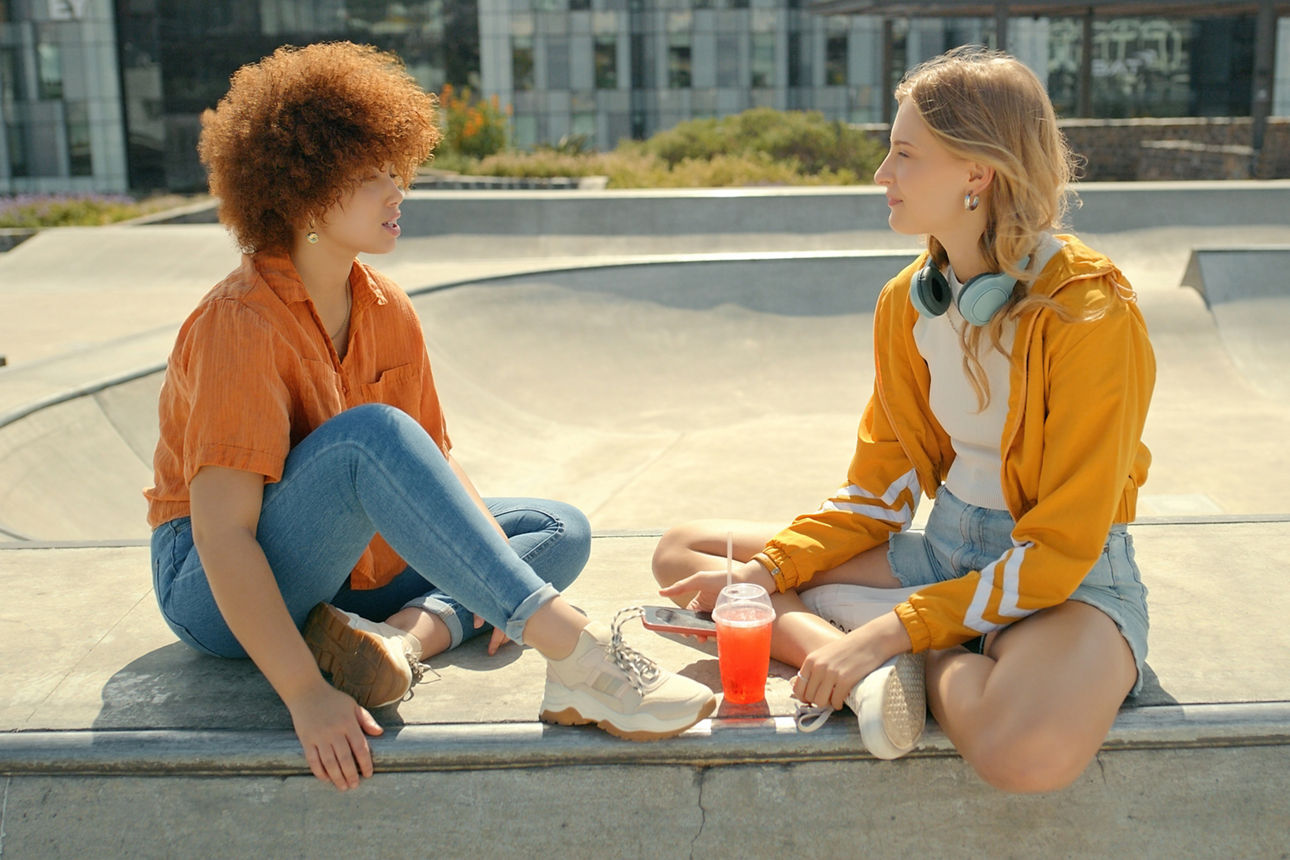 Zwei junge Frauen, die sich bei einem Skatepark unterhalten.