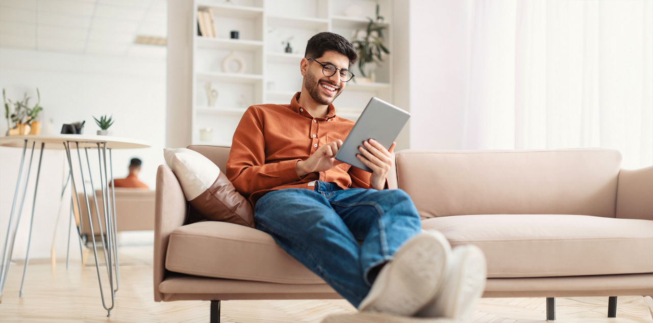 Mann sitzt mit einem Tablet auf der Couch