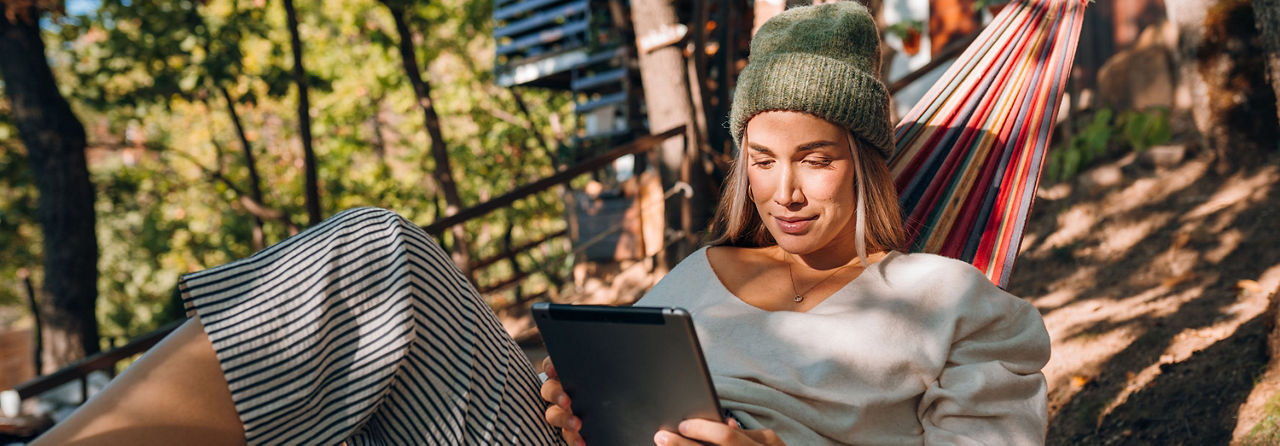 Frau liegt gemütlich in der Hängematte und liest den Newsletter am Tablet.