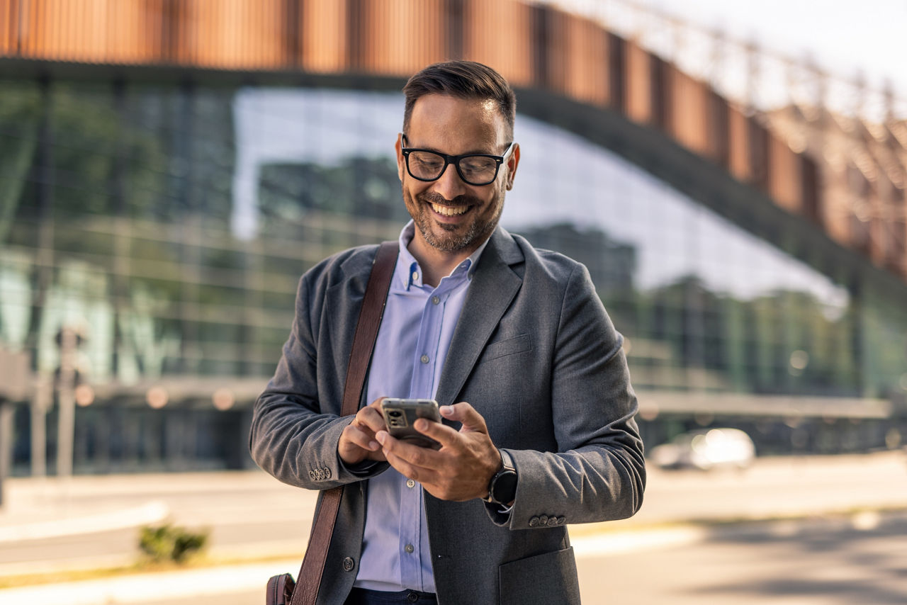 Mann steht mit seinem Smartphone vor einem Gebäude und lacht
