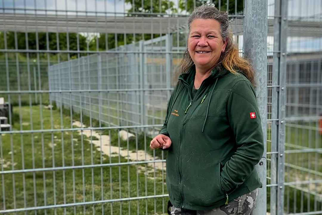 Frau Gruber in grüner Fleecejacke steht rechts im Bild, im Hintergrund Gitter zu den Hundezwingern