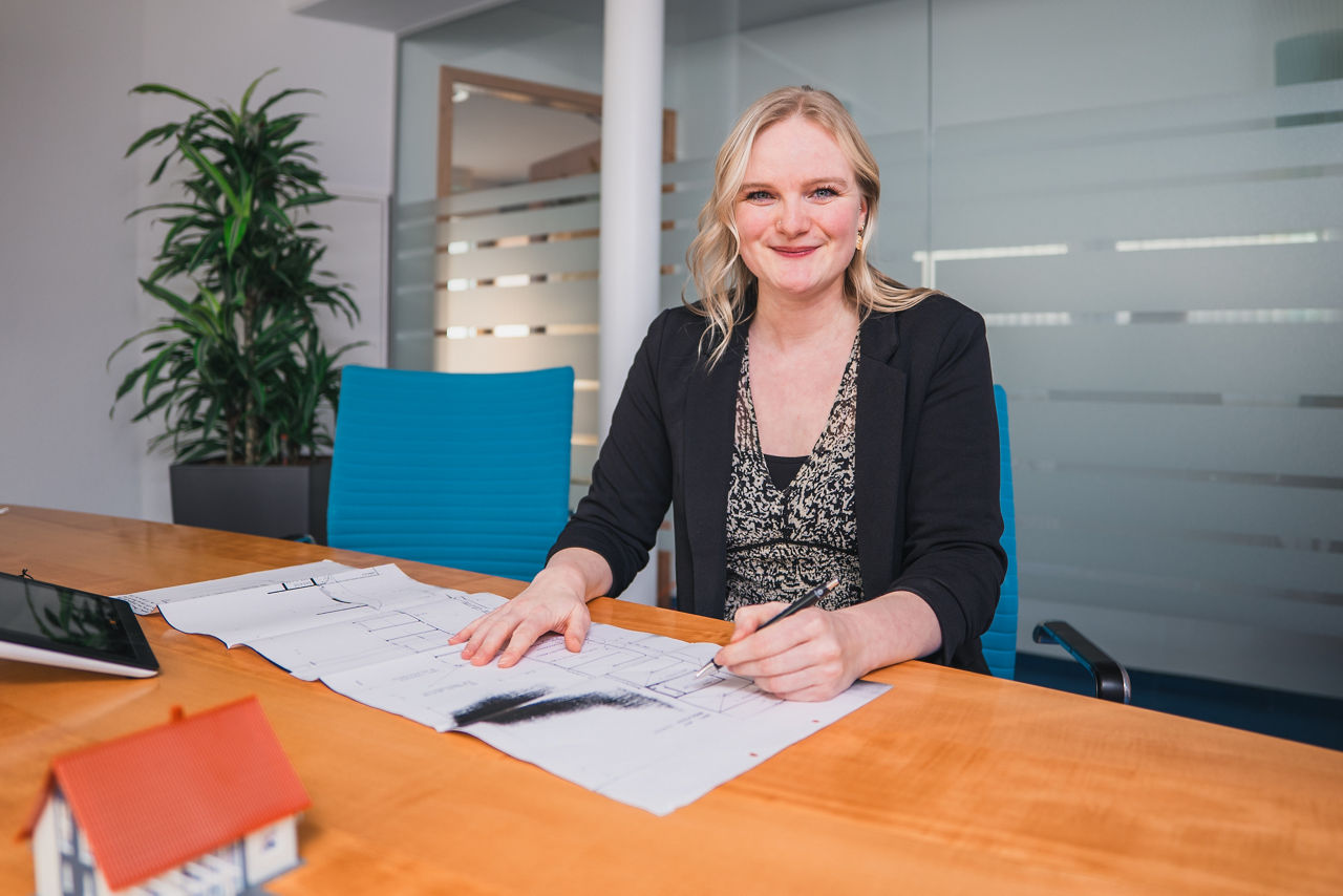 Frau Laufer sitzt am Tisch mit einem Bauplan und einem Modellhaus