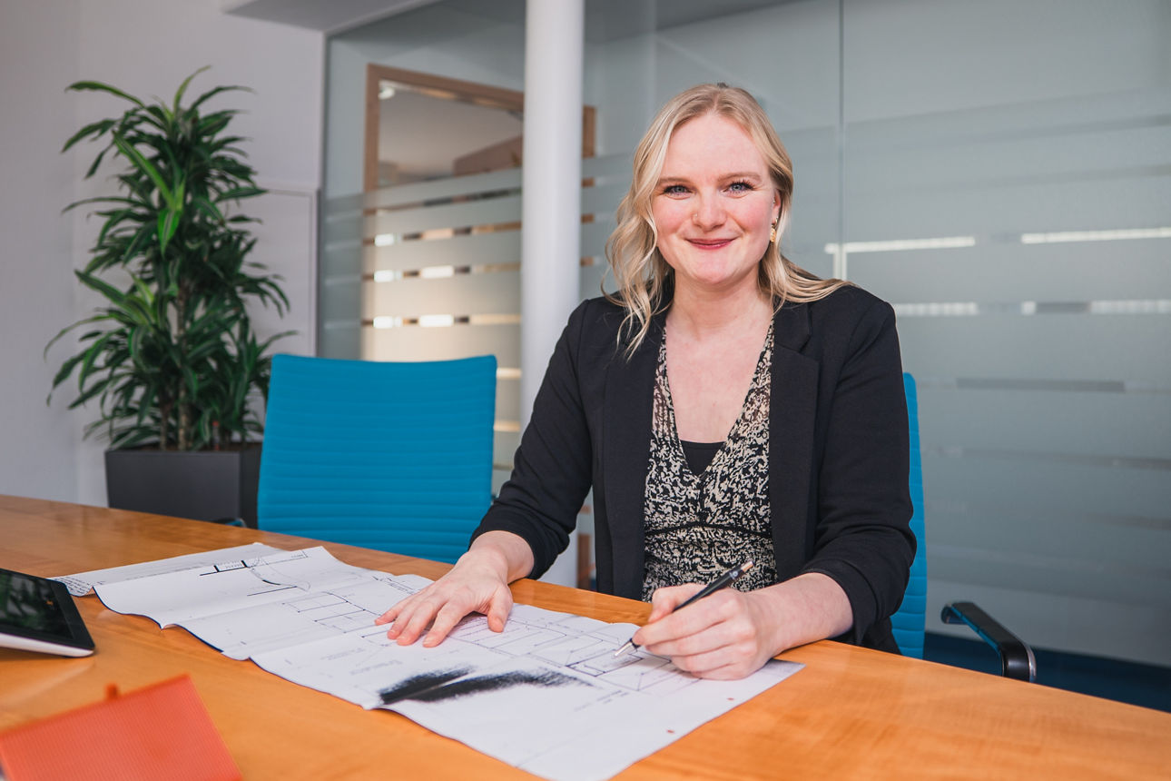 Frau Laufer sitzt am Tisch mit einem Bauplan und einem Modellhaus