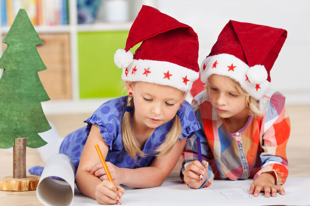 Zwei Kinder mit Nikolausmützen malen gemeinsam auf dem Boden.